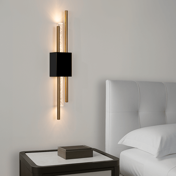 Modern wall sconce with black and gold design on a neutral wall next to a bed.